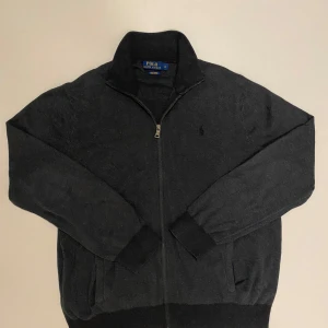 Svart Ralph Lauren zip - Säljer en stilren mörkgrå tröja från Ralph Lauren i Pima bomull. Tröjan har en dragkedja framtill och långa ärmar. Den klassiska loggan är diskret broderad på bröstet. Perfekt för en avslappnad men elegant look. Tröjan är i perfekt skick och skriv vid minsta fråga eller fundering💯👍