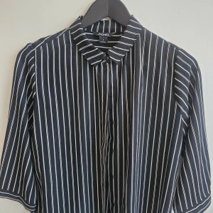 Svartvit randig skjorta från Monki - Snygg svart skjorta från Monki med vita ränder och knappar framtill. Skjortan har trekvartsärmar och en klassisk krage. Perfekt för en stilren look.