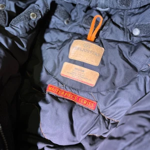 Svart Parajumpers Jacka, M - Säljer en snygg svart parkajacka från Parajumpers Masterpiece Series. Nypris ca 12000 kr. Jackan har flera fickor, en huva och en cool patch på ärmen. Perfekt för kyliga dagar med sin långa design och praktiska detaljer. Som sagt många fickor, på bilden ser den mörkblå ut men det är bara lampan annars är den svart. Medium. Kan ha fläckar, lite smutsig.