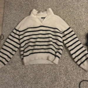 Vit och svart randig tjocktröja - Säljer en snygg vit tröja med svarta ränder. Tröjan har en v-ringad krage och långa ärmar. Perfekt för en stilren look.