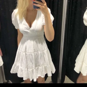 Vit klänning från Zara - Charmig vit klänning från Zara med kort ärm och v-ringad design. Klänningen har en volangdetalj vid fållen och en smickrande passform som markerar midjan. Perfekt för sommarens alla tillfällen. Perfekt till studenten!❤️priset kan diskuteras! Använd 1 gång