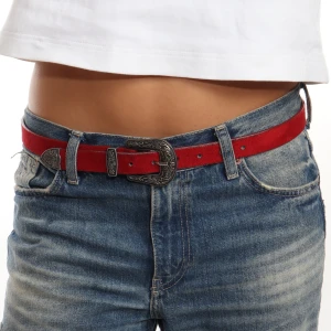Rött mockabälte med detaljerad spänne - Snyggt rött bälte i mocka med ett detaljerat metallspänne. Perfekt för att ge en färgklick till din outfit. Passar bra till jeans och andra casual kläder.