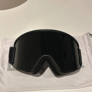 Svarta skidglasögon från EQPE - Snygga svarta skidglasögon från EQPE med bred elastisk rem för bekväm passform. Perfekta för vintersport och skyddar effektivt mot bländning. Kommer med en praktisk förvaringspåse. Använda i två säsonger.