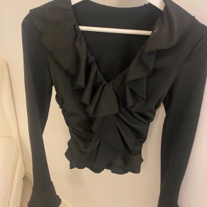 Svart topp från shein - En svart festlig topp från shein. Den har långa ärmar med volanger längst ner. En vringad med volanger ner till bröstet. 