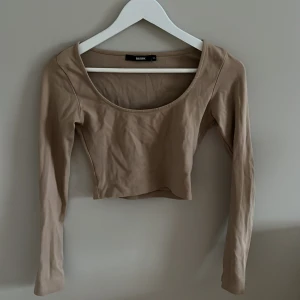 Beige croppad topp från Bik Bok - Snygg beige croppad topp från Bik Bok med långa ärmar och rund halsringning. Perfekt för en stilren look.