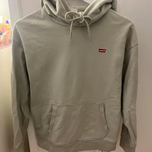 Mint grön hoodie från Levi's - Säljer en stilren mint grön hoodie från Levi's med klassisk känguruficka och justerbar huva. Inte så väl andvänd och i bra skick. Den har en liten röd Levi's-logga på bröstet.