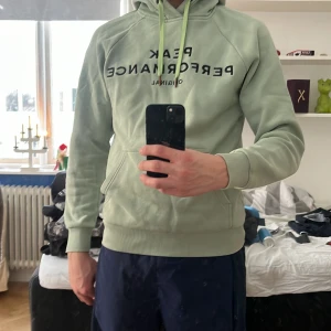 Grön hoodie från Peak Performance - Säljer en grön hoodie från Peak Performance med svart text på bröstet. Perfekt för en avslappnad stil. Använd enstaka gånger utan större defekter. Pris kan diskuteras!
