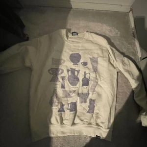 Beige sweatshirt från Vintage Supply - Säljer en vit  sweatshirt från Vintage Supply med ett unikt tryck av olika vaser och kannor i mörkblått. Tröjan har en avslappnad passform och rund halsringning. Perfekt för en stilren och bekväm look.