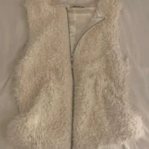 Vit pälsväst från Gina Tricot - Säljer en fluffig vit pälsväst från Gina Tricot med dragkedja framtill. Perfekt för att hålla sig varm och stilren under kyligare dagar. Den är i storlek S 💗