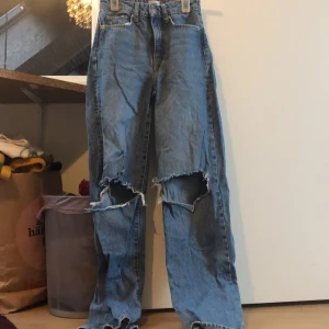 Blå jeans med slitningar från 157 Boulevard - Säljer ett par blå jeans från 157 Boulevard med coola slitningar på knäna och en avslappnad passform. Perfekta för en trendig och avslappnad stil. De har en klassisk femficksdesign och är tillverkade i denim.