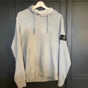 Grå hoodie från Stone Island - Säljer en stilren grå hoodie från Stone Island med klassisk logga på ärmen. Tröjan har en bekväm passform med långa ärmar och en praktisk huva med dragsko. Perfekt för en avslappnad look.
