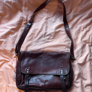 Axelväska i läder - Säljer en snygg brun axelväska i skinn från Gusti Leder. Väskan har ett justerbart axelband och ett stort fack som rymmer en laptop. Perfekt för både skola och jobb!