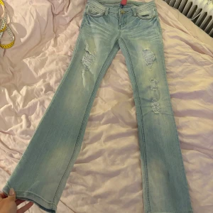 Ljusa blåa jeans med slitningar - Snygga ljusblå lågmidjade bootcut jeans med slitningar på framsidan