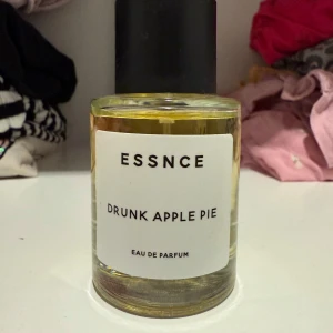 Essnce Drunk Apple Pie Eau de Parfum - Upptäck Essnce Drunk Apple Pie, en Eau de Parfum med en unik doft av äppelpaj och kryddor. Flaskan är rund med en enkel vit etikett och svart kork. Perfekt för dig som vill ha en söt och kryddig doftupplevelse. 
