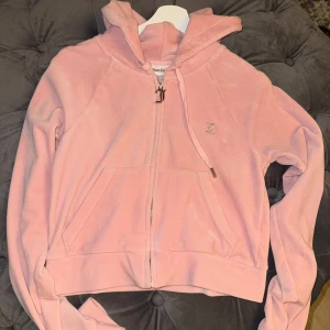 Rosa hoodie från Juicy Couture - Säljer en rosa hoodie från Juicy Couture med dragkedja och huva. Den har glittrande text på ryggen och vita ränder längs ärmarna. Använd några få gånger ,äkta såklart 
