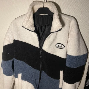 Flerfärgad teddyjacka med dragkedja - Varm vinterjacka/kofta. Perfekt nu på vintern. Den är vit, svart och blå. Långa ärmar och dragkedja. Köpt för 800 kr. 