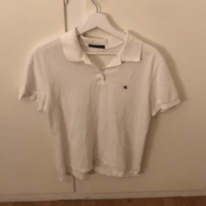 Vit pikétröja från Mobaco Cottons - Säljer en klassisk vit pikétröja från Mobaco Cottons med en liten broderad logga på bröstet. Tröjan har korta ärmar och en traditionell krage. Perfekt för en stilren och avslappnad look.