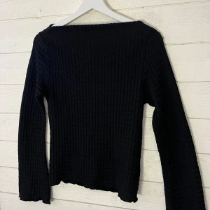 Svart  tröja - Säljer en svart ribbad tröja med långärmad design. Tröjan har en unik textur och en bekväm passform som passar perfekt för kyligare dagar. Perfekt för att lägga till en stilren touch till din garderob.