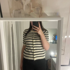 Randig kofta med knappar - Säljer en stilren randig kofta i svart och vit med knappar framtill. Koftan har korta ärmar och en klassisk design som passar perfekt till både jeans och kjol. (Den är helt oanvänd fast det finns ingen lapp kvar).