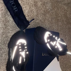 Dior b22 - Snygga svarta sneakers från Dior med vita detaljer och snörning. Skorna har en modern design med reflekterande element och kommer i originalförpackning. Priset kan diskuteras