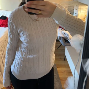 Vit kabelstickad tröja - Säljer en stilren vit kabelstickad tröja med rund hals och långa ärmar. Perfekt för kyligare dagar och lätt att matcha med olika outfits.