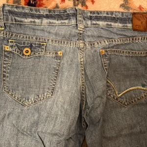 Blå jeansshorts från STF - Blåa halvlånga med cool knapp- och broderi design på bak- och framfickan. Midjemåttet är 80cm och längd på inre ben är 36cm