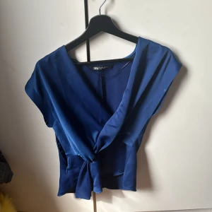 Blå omlottopp från Zara - Snygg blå omlottopp från Zara med knytning framtill. Perfekt för en stilren look. Tillverkad i ett mjukt material som ger en bekväm passform.