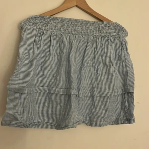 Randig kjol från H&M - Säljer en söt randig kjol från H&M i blått och vitt. Kjolen har en elastisk midja och dubbla lager för en luftig känsla. Perfekt för varma dagar!