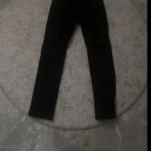 Svarta jeansbyxor - Snygga svarta jeansbyxor med en klassisk design. De har en rak passform och är perfekta för en stilren look. Byxorna har knappar och dragkedja framtill.