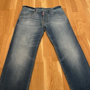 Blå jeans från Dsquared2 - Snygga blå jeans från Dsquared2 med klassisk femficksdesign och en diskret tvättad look. De har en knappgylf och en röd etikett vid gylfen. Perfekta för en avslappnad stil. Dem är köpt från kids brand store för 2000 kr och är i storlek 14 vilket motsvarar 31:30 passar mig bra bara lite större än valkng då jag gillar slim och dem här är regular fit vid benen