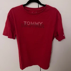 Röd t-shirt från Tommy Hilfiger - Snygg röd t-shirt från Tommy Hilfiger med logotypen tryckt på bröstet. T-shirten har en klassisk rund hals och korta ärmar. Perfekt för en avslappnad stil. S passar M