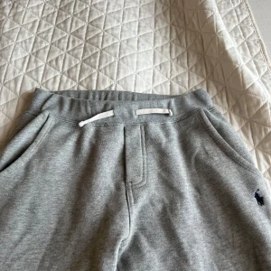 Grå mjukisbyxor från Ralph Lauren - Snygga och bekväma grå mjukisbyxor från Ralph Lauren med elastisk midja och snörning. Byxorna har en broderad logotyp på sidan och är perfekta för en avslappnad stil. Hör av dig vid intresse kan gå att diskutera pris. Skick 7/10 Inga skador Inga hål.