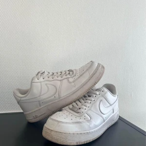 Vita Nike Air Force 1 - Säljer ett par klassiska vita Nike Air Force sneakers. De är i välanvänt skick men fortfarande superbekväma och stilrena. Perfekta för vardagsbruk och passar till nästan allt i garderoben. Storlek är inte angiven, men de ser ut att vara i en standard herrstorlek.