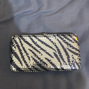 Glittrig zebramönstrad plånbok - Snygg och glittrig plånbok med zebramönster. Perfekt för att ge lite extra stil till din outfit. Plånboken har flera kortfack och en dragkedjeficka för mynt. Den är både praktisk och trendig, idealisk för festliga tillfällen.