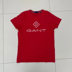 Röd t-shirt från GANT - Säljer en snygg röd t-shirt från GANT i bomull. Den har en klassisk passform med korta ärmar och ett stilrent tryck med GANT-loggan på framsidan. Perfekt för både vardag och fest! 🔥