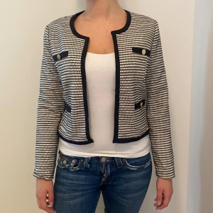 Randig kavaj från Stockh lm - Snygg och stilren randig kavaj från Stockh lm i svart och vit. Den har långa ärmar och dekorativa knappar framtill. Perfekt för både vardag och fest. Passar bra till jeans eller kjol för en chic look. Storlek 38