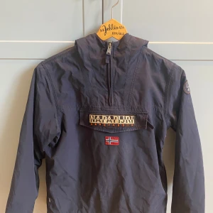 Napapijri jacka - Anorak i fint skick. Mindre skador i tyget på framsidan, se bild. Fodrad med fleece. Storlek 152 cm, 12 år.