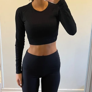 Aim’n svart ribbad croppad topp - Säljer en snygg Aim’n svart ribbad croppad topp med långa ärmar. Perfekt för träning eller en casual look. Toppen är tight och bekväm, och passar bra till både leggings och jeans. Ett måste i garderoben för alla som älskar stil och komfort!