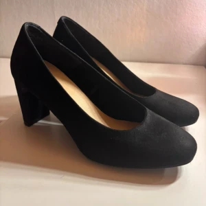 Svarta mockapumps med klack - Säljer ett par eleganta svarta klackar i mocka. De har en bekväm klack och en klassisk design som passar perfekt för både vardag och fest. Skorna är i bra skick endast använda under en kväll 