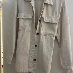 Beige overshirt från Bik Bok - Säljer en superfin beige overshirt från Bik Bok i storlek XS. Den har långa ärmar och knappar framtill, samt två stora fickor på bröstet. Materialet känns som bomull och den har ett bälte i midjan för en snygg passform. Perfekt nu till höst!