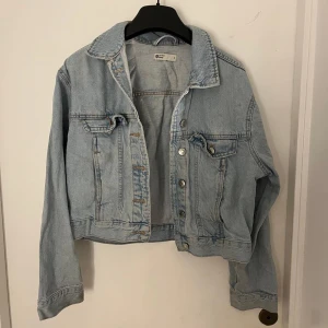 Ljusblå croppad jeansjacka - Säljer en snygg ljusblå croppad jeansjacka från H&M. Den har en klassisk krage och knappar framtill. Perfekt för vår och sommar, och funkar både till vardags och fest. Jackan har två bröstfickor med knappdetaljer.