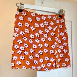 Orange minikjol med blommor och liten slits, i tunt tyg 