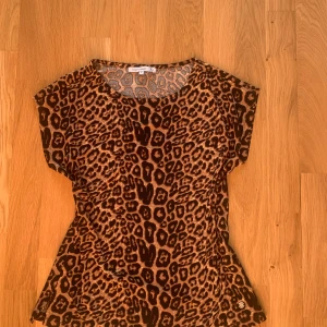 Leopard topp med korta armar - Supersnygg fest-topp/höst-topp i leopard mönster med korta armar som slutar direkt över axeln. Passar perfekt till en kort kjol och höga klackar och materialet är tunt och skönt! Längst ner på tröjan sitter en snygg, rund gulddetalj.  