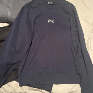 Mörkblå tröja från Emporio Armani - Snygg mörkblå tröja från Emporio Armani med EA7-logga på bröstet. Tröjan är helt oanvänd då den ej passar, den är i storlek Large herr, vid frågor eller funderingar är det bara höra av sig