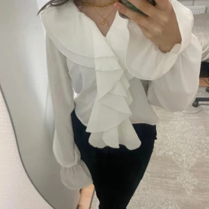 Volangblus - Vit blus med volanger och snören som man knyter ihop. Helt oanvänd med prislappen på.