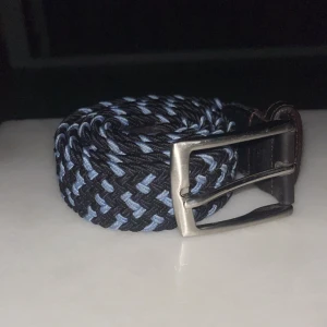 Flätat bälte från Howard London - Snyggt flätat bälte från Howard London i svart och blått. Bältet har tt klassiskt silverfärgad spänne och är 90 cm långt. Perfekt för att ge en stilren touch till din outfit. Är även ett riktigt fint och lyxigt märke och bälte nypris 499 kr, mitt pris 159 kr👊🏼🔥