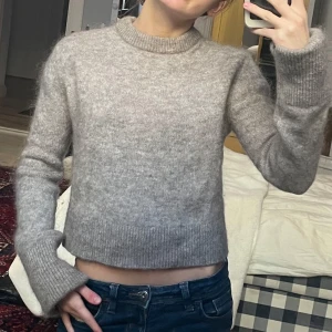 Mohair stickad tröja - Säljer en mysig beige stickad tröja med rund hals och långa ärmar. Perfekt för kyliga dagar. Tröjan har en croppad passform som ger en modern look. Passar bra till jeans eller kjol.
