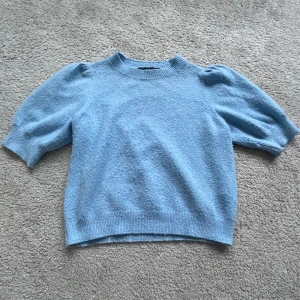 Blå stickad tröja från Vero Moda - Säljer en ljusblå stickad tröja från Vero Moda med korta puffärmar och ribbade kanter. Perfekt för en stilren look. Tröjan är mjuk och bekväm, idealisk för både vardag och speciella tillfällen. Passar perfekt till jeans eller kjol. Passar som S 