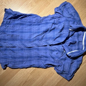 Blå rutig skjorta från Bergans - Säljer en blå rutig skjorta från Bergans med korta ärmar och knappar framtill. Skjortan har en broderad logga på bröstet och är tillverkad i ett lätt material.🔥🤞🏻