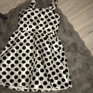 Prickig klänning med axelband - Säljer en söt klänning med stora svarta prickar på vit bakgrund. Klänningen har breda axelband och en klassisk passform som ger en fin siluett. Den är lite gul i armhålorna men syns inte lika mycket i verkligheten. Även några små, små fläckar. Kan skicka bild om någon är intresserad. 